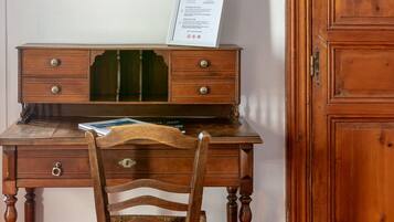 A wooden desk with drawers, a chair with a woven seat, a framed picture on the wall, and a wooden cabinet.