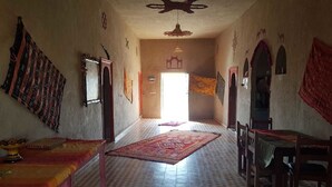 A room with a checkered floor, a central rug, and a table with a red tablecloth. - Riad Desert Camel (Taouz)
