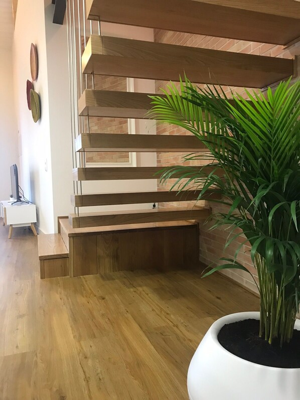 A wooden staircase with a modern design, a potted plant, and a white side table with a lamp. - Porta 20 - Vacation Home (Loulé)