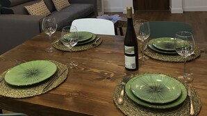 A dining area with a wooden table set for four, green plates, and wine glasses. A painting is on the wall, and there is a sofa in the background. - Porta 20 - Vacation Home (Loulé)
