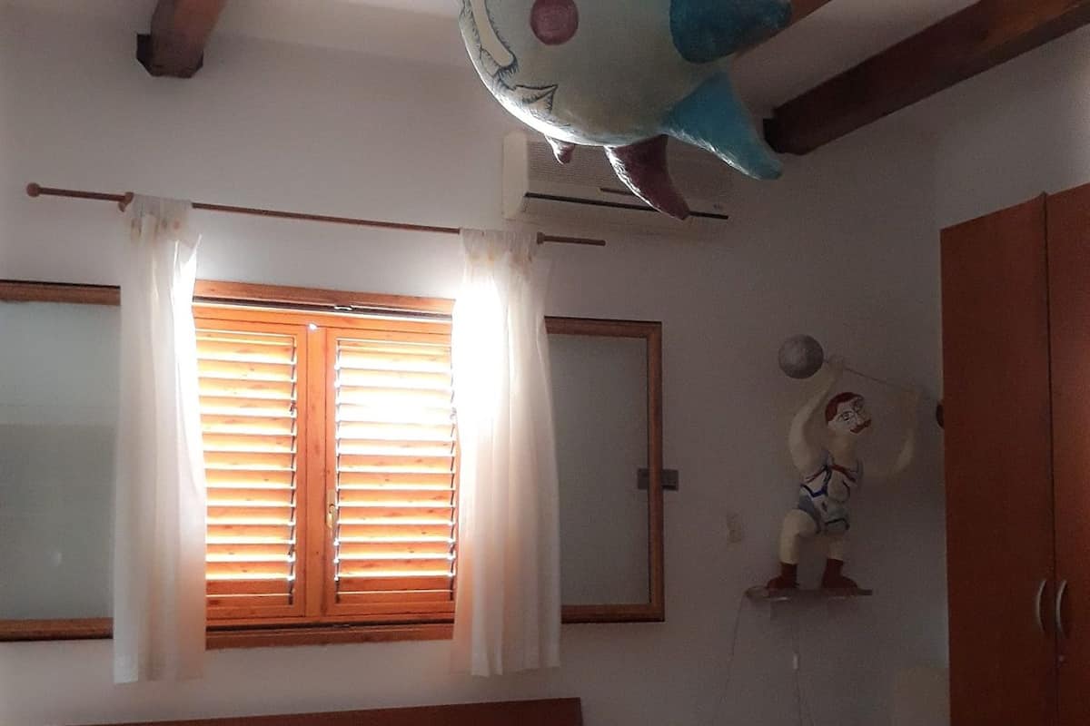 Une chambre à coucher comprenant un lit, une fenêtre avec des stores, un climatiseur fixé au mur, un élément de décoration murale et une armoire.