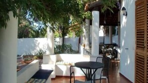 A patio area with a table and chairs, a white wall, and a wooden shutter.