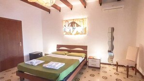 A bedroom with a bed, a nightstand, a wall-mounted air conditioner, and a painting above the bed.