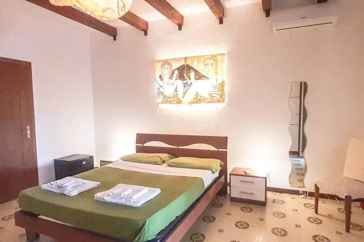 Une chambre à coucher comprenant un lit, une table de chevet, un climatiseur fixé au mur et un tableau au-dessus du lit.