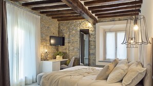 Ein Schlafzimmer mit Steinwand, einem Bett mit weißer Bettwäsche, einem Nachttisch mit Kerze und einem an der Wand montierten Fernseher.