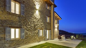 Ein Gebäude aus Stein mit zahlreichen Fenstern, einem Balkon mit Tisch und Stühlen und Blick auf die Landschaft.