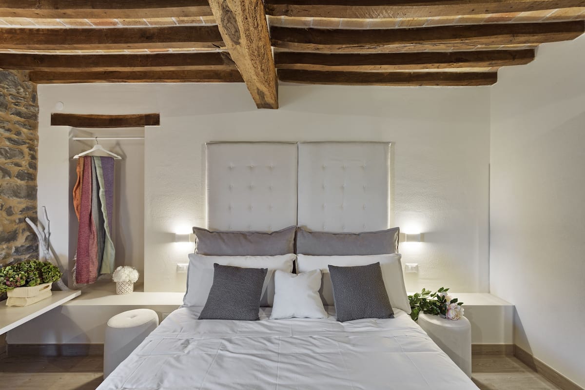 A bedroom with a large bed, two bedside tables, a hanging garment rack, and a stone wall.