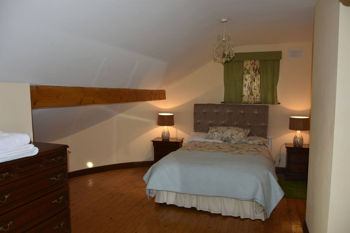 A bedroom with a large bed, wooden headboard, two bedside tables with lamps, a dresser, and a chandelier.