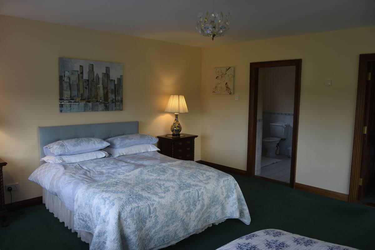 A neatly made bed with a patterned bedspread, a bedside lamp, and a cityscape painting on the wall.