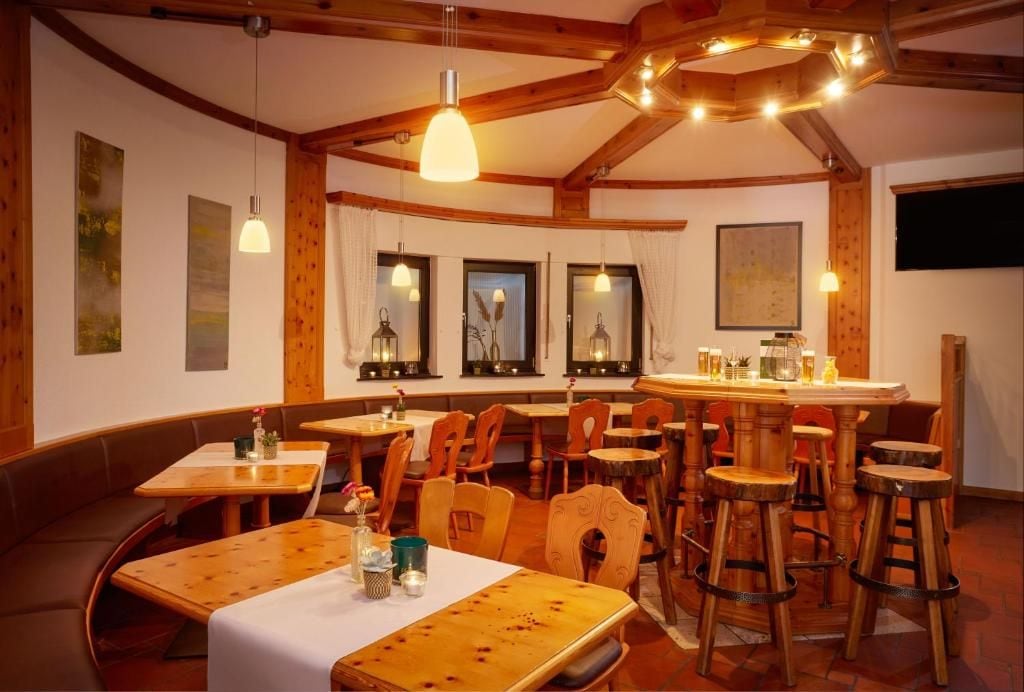 A restaurant interior with wooden tables and chairs, pendant lighting, and a bar area.