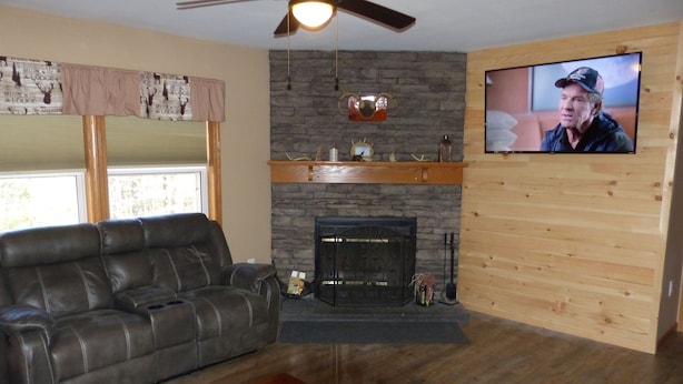 Una sala de estar con sofá de cuero, chimenea, televisor y ventilador de techo.