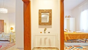 A hotel room with a marble floor, a bed with a yellow bedspread, a wooden-framed mirror, and a small decorative shelf with a golden statue. - DolceVita Apartments N. 250 (Venice)