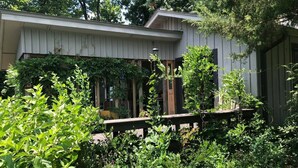 A house with a covered porch, surrounded by dense greenery and a wooden fence. - Shepherds Retreat - 2 miles to I-65 (Montevallo)