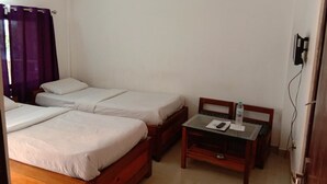 Une chambre avec deux lits simples, une petite table avec une chaise et une fenêtre ornée de rideaux violets.