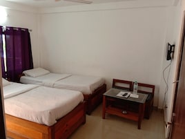 A room with two single beds, a small table with a chair, and a window with purple curtains.