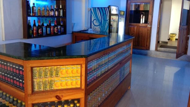 Un espace bar avec des étagères remplies de bouteilles d’alcool, un réfrigérateur et un comptoir en bois où sont présentés des fruits.