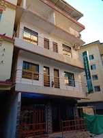 A multi-story hotel with balconies, a green signboard, and a covered entrance.
