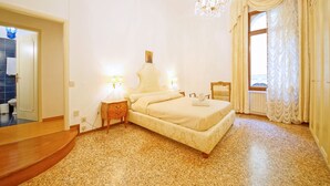 Een slaapkamer met een bed, bedlampen, een kroonluchter en een raam met gordijnen.
