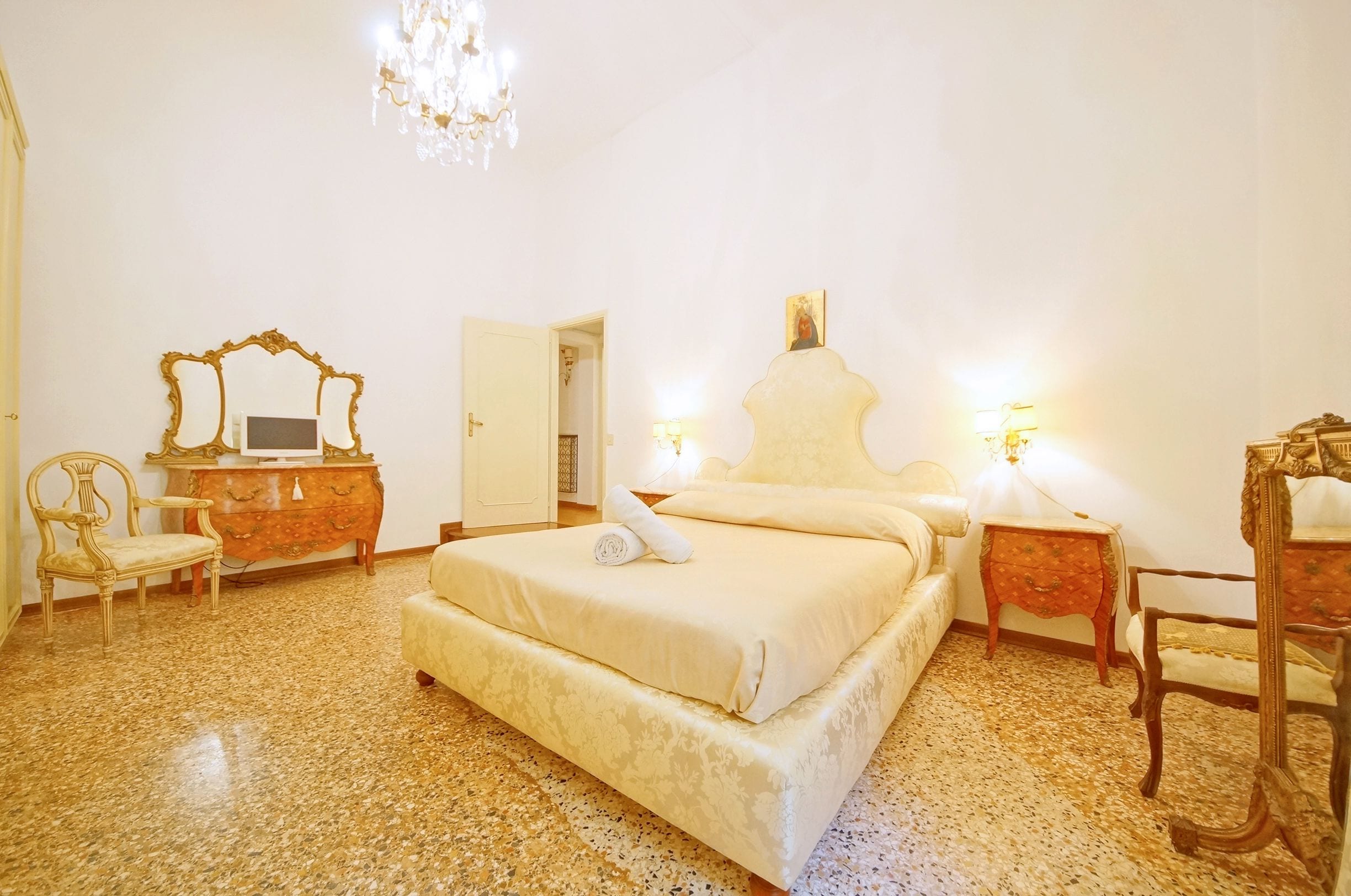 Een hotelkamer met een groot bed, een dressoir, een stoel en een kroonluchter.