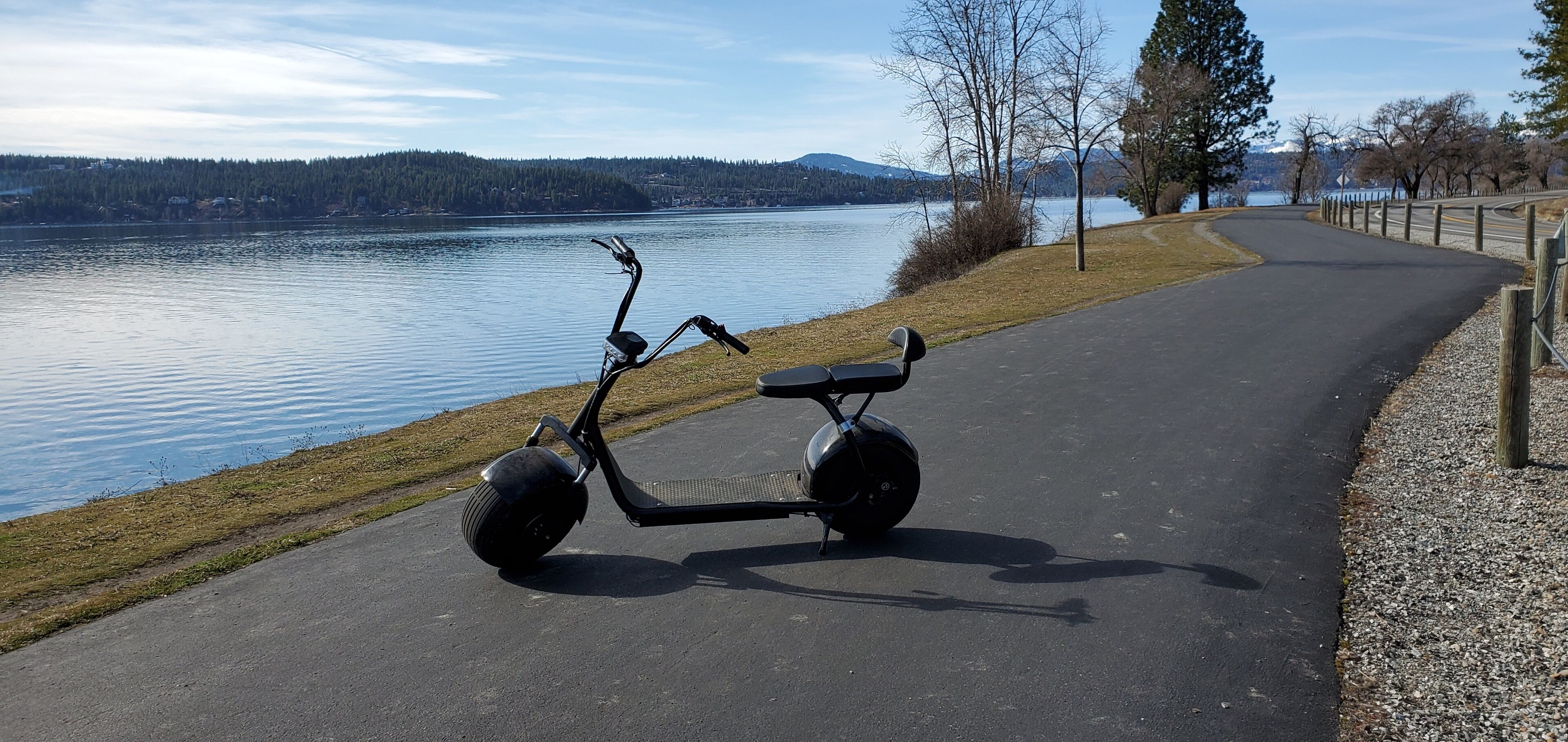 Een stilstaande elektrische scooter op een verhard pad langs een meer.
