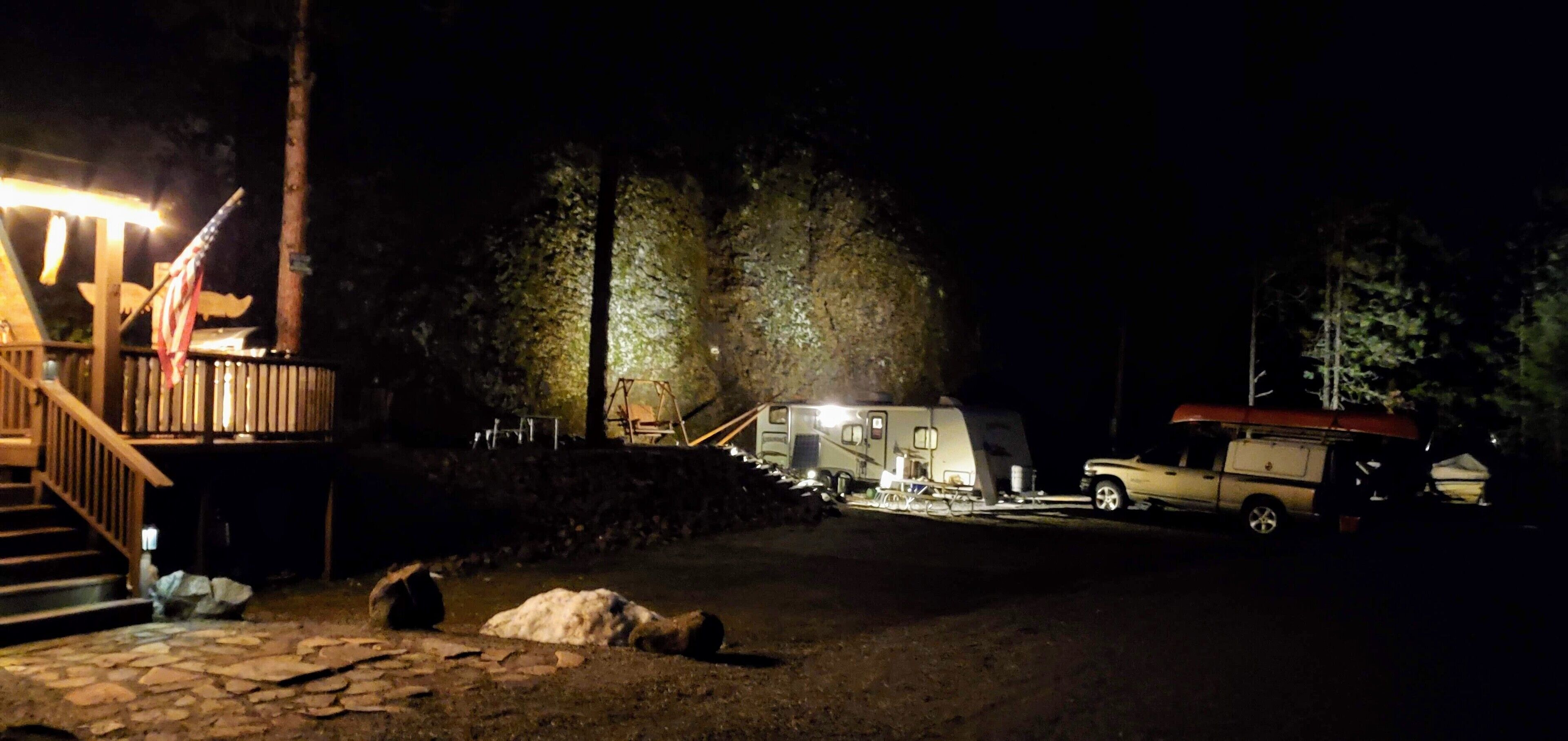 Un camping de noche con una terraza de madera, una zona cubierta y una caravana.
