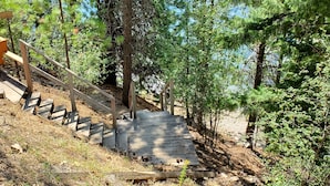 Un escalier en bois menant au sommet d’une colline, entouré d’arbres et agrémenté d’un banc en bois.
