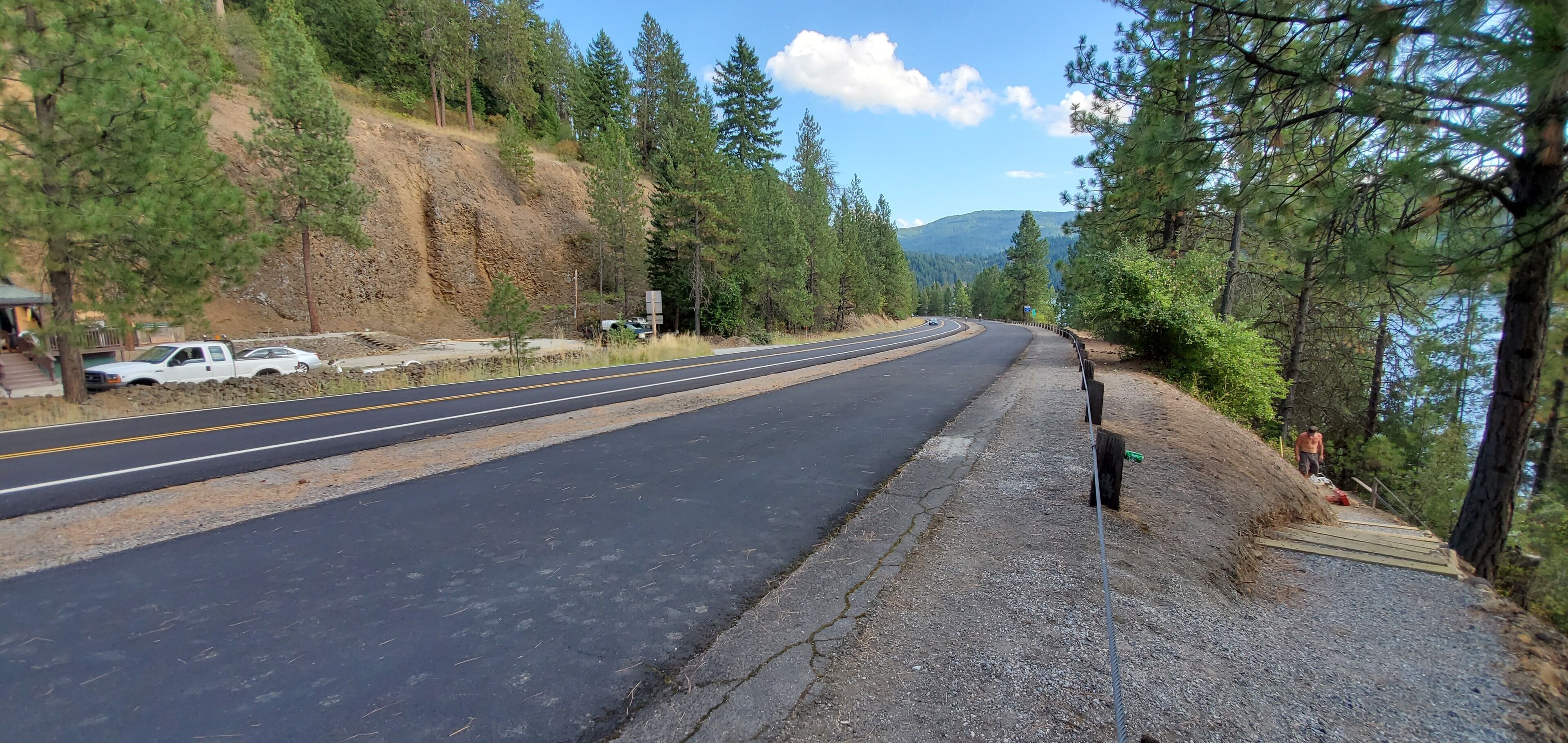 A road curving through a forested area with a white truck parked on the side.