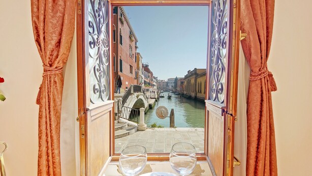 Ein Zimmer mit Blick auf einen Kanal, ein Tisch mit zwei Weingläsern und Vorhängen.