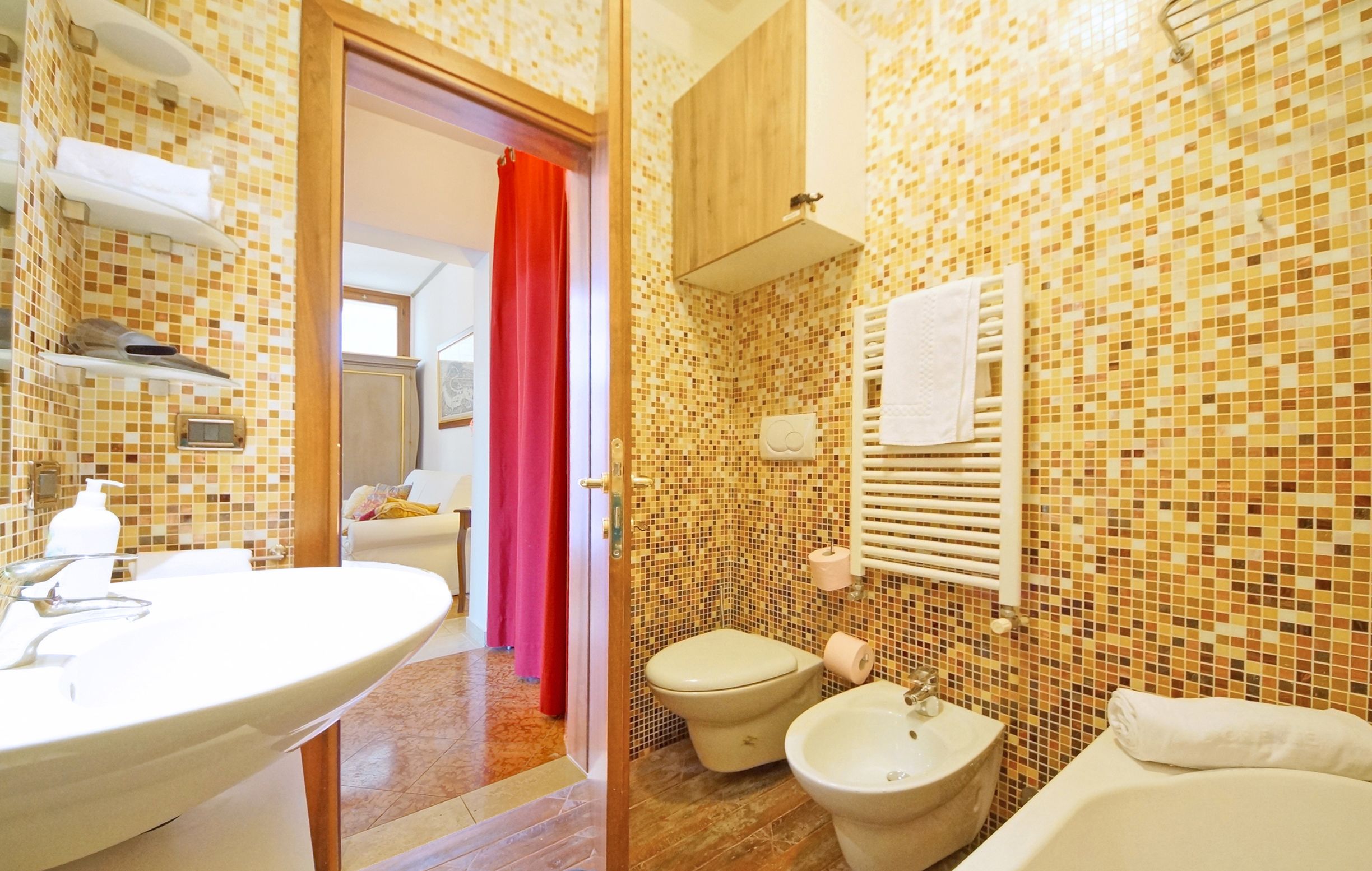 Ein Badezimmer mit mosaikbesetzten Wänden, einem weißen Waschbecken, einem Bidet, einer Toilette und einer Badewanne.