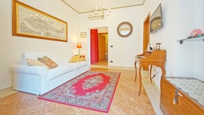 Ein Wohnzimmer mit einem weißen Sofa, einem roten Teppich mit Muster, einem Holzpiano, einer Holzkabine und einer gerahmten Karte an der Wand.