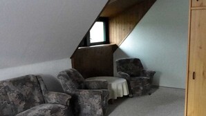 Una habitación con techo inclinado, un armario de madera y dos sillones con una mesita redonda.