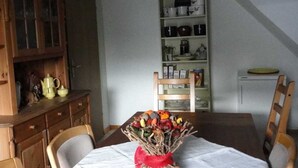 Un comedor con una mesa preparada para cuatro, un aparador de madera con puertas de cristal y una estantería en la pared.