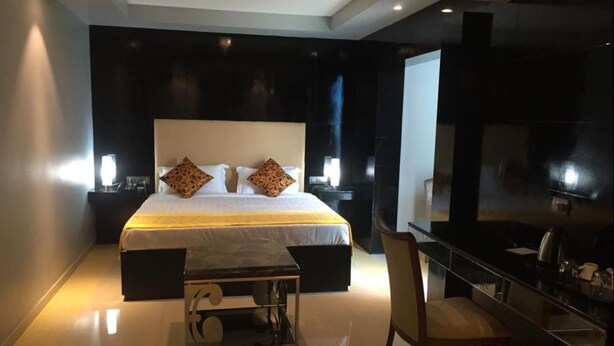 A modern hotel room with a large bed, bedside tables with lamps, a desk with a chair, and a TV on the wall. - Le Raj Courtyard (Gummidipundi)