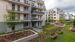 Een meerlaags woongebouw met balkons, een aangelegde tuin met bankjes, en een heldere lucht.