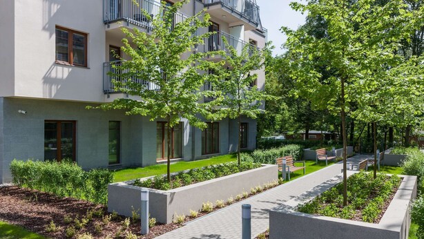 Een modern appartementencomplex met balkons, een aangelegde tuin en een verharde looppad.