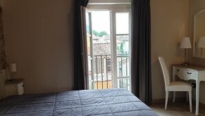 A bedroom with a bed, a desk, and a chair. There is a window with curtains, and a balcony is visible outside. - B&B Il Tiglio (Lucca)