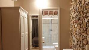 A bedroom with a bed, a wardrobe, a desk, and a stone wall. - B&B Il Tiglio (Lucca)