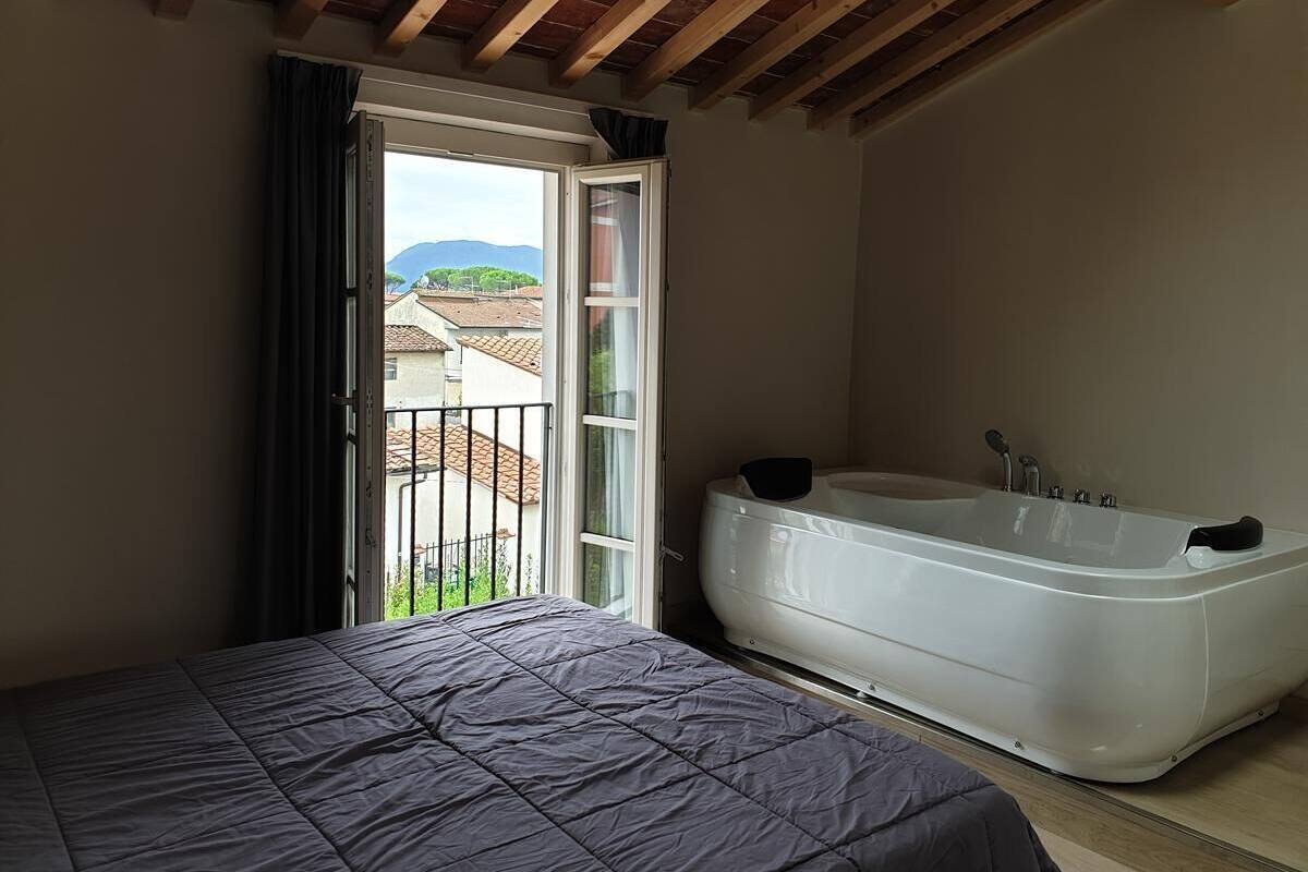 A bedroom with a large bed, a bathtub, and a balcony with a view of buildings and mountains.