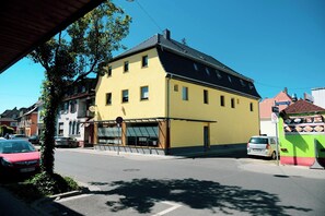 A yellow building with a black roof, a visible storefront, and a street with parked cars. - Pension und Monteurzimmer VICTORIA (Ludwigshafen)