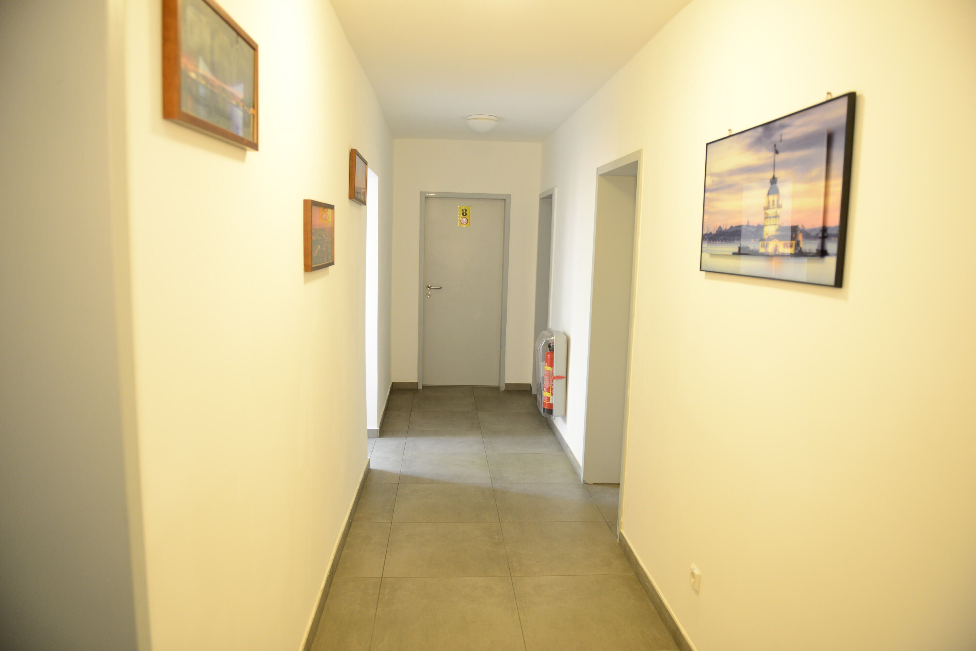 A hallway with framed pictures on the walls, a door at the end, and a fire extinguisher on the right.