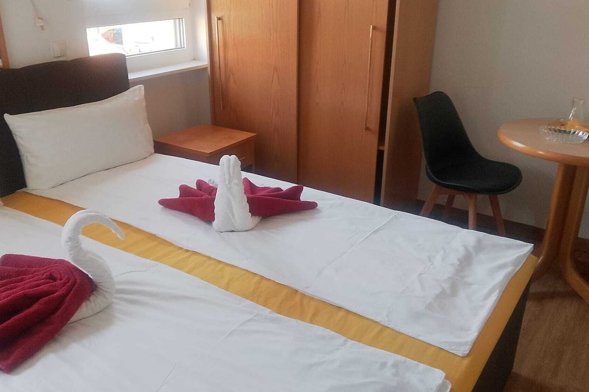 A hotel room with a bed, a chair, a small table, and a wardrobe.