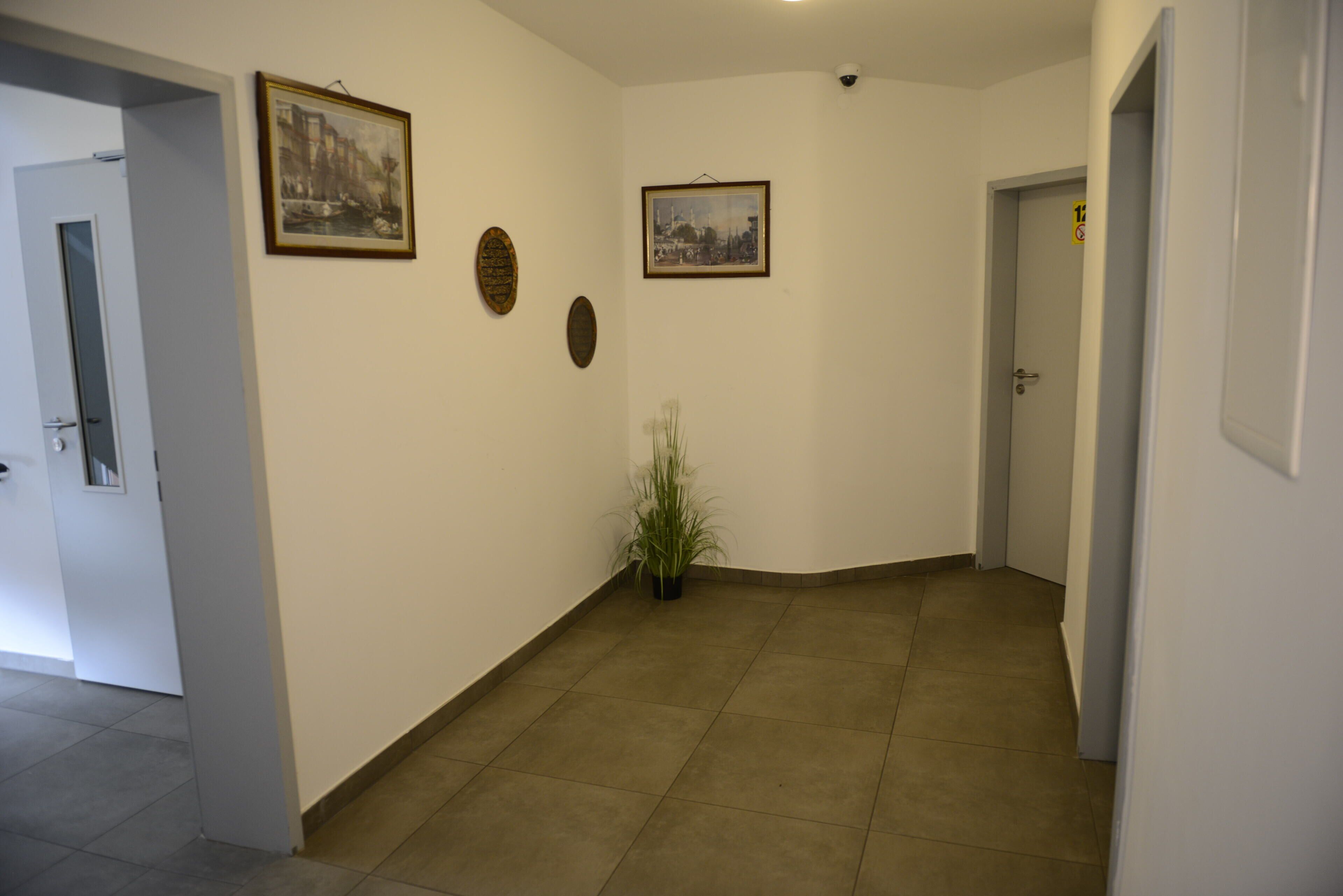 A hallway with a potted plant, two framed pictures, and a door with a sign.