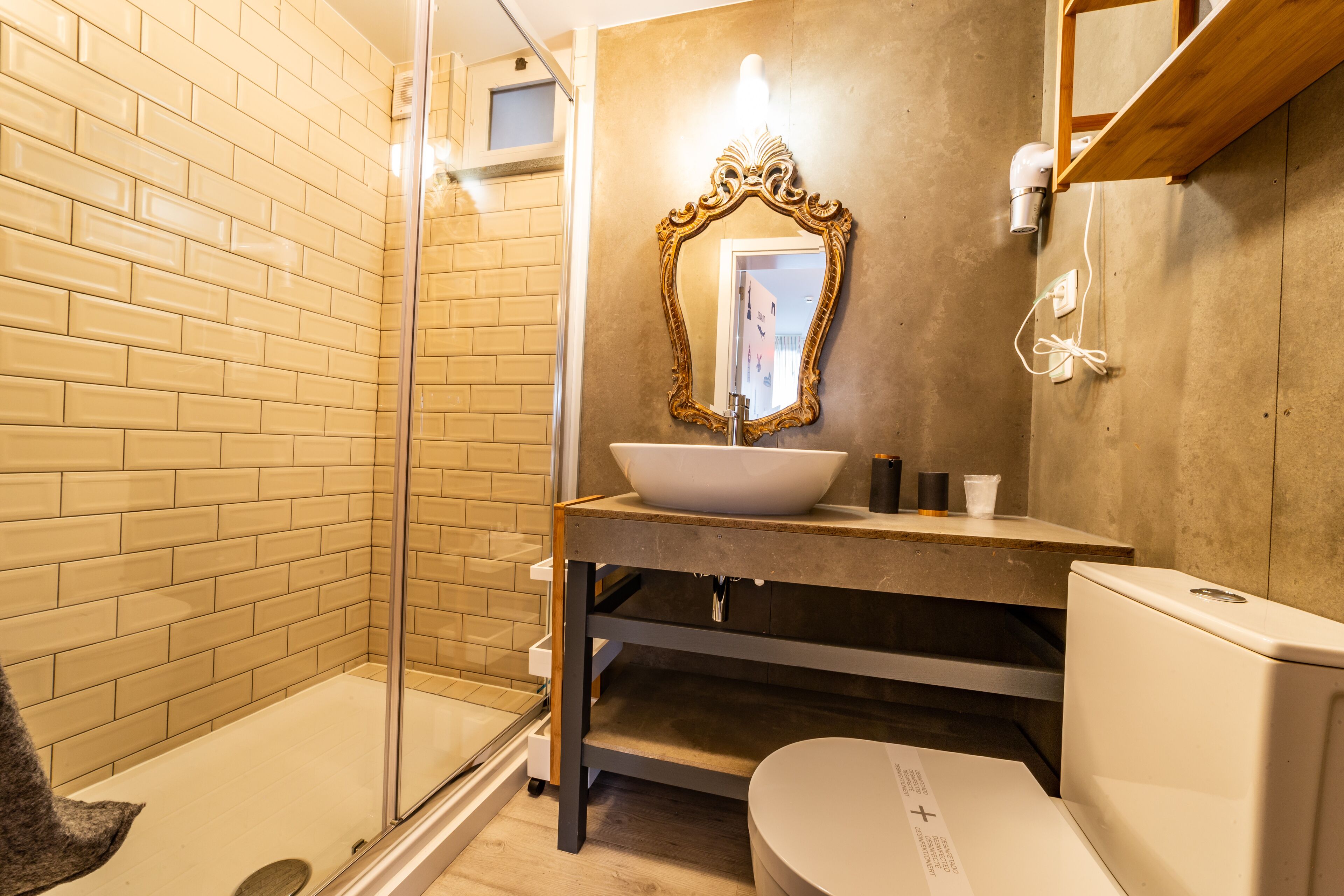 A bathroom with a glass shower enclosure, a white sink with a gold-framed mirror, and a white toilet.
