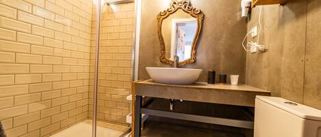 A bathroom with a glass shower enclosure, a white sink with a gold-framed mirror, and a white toilet.