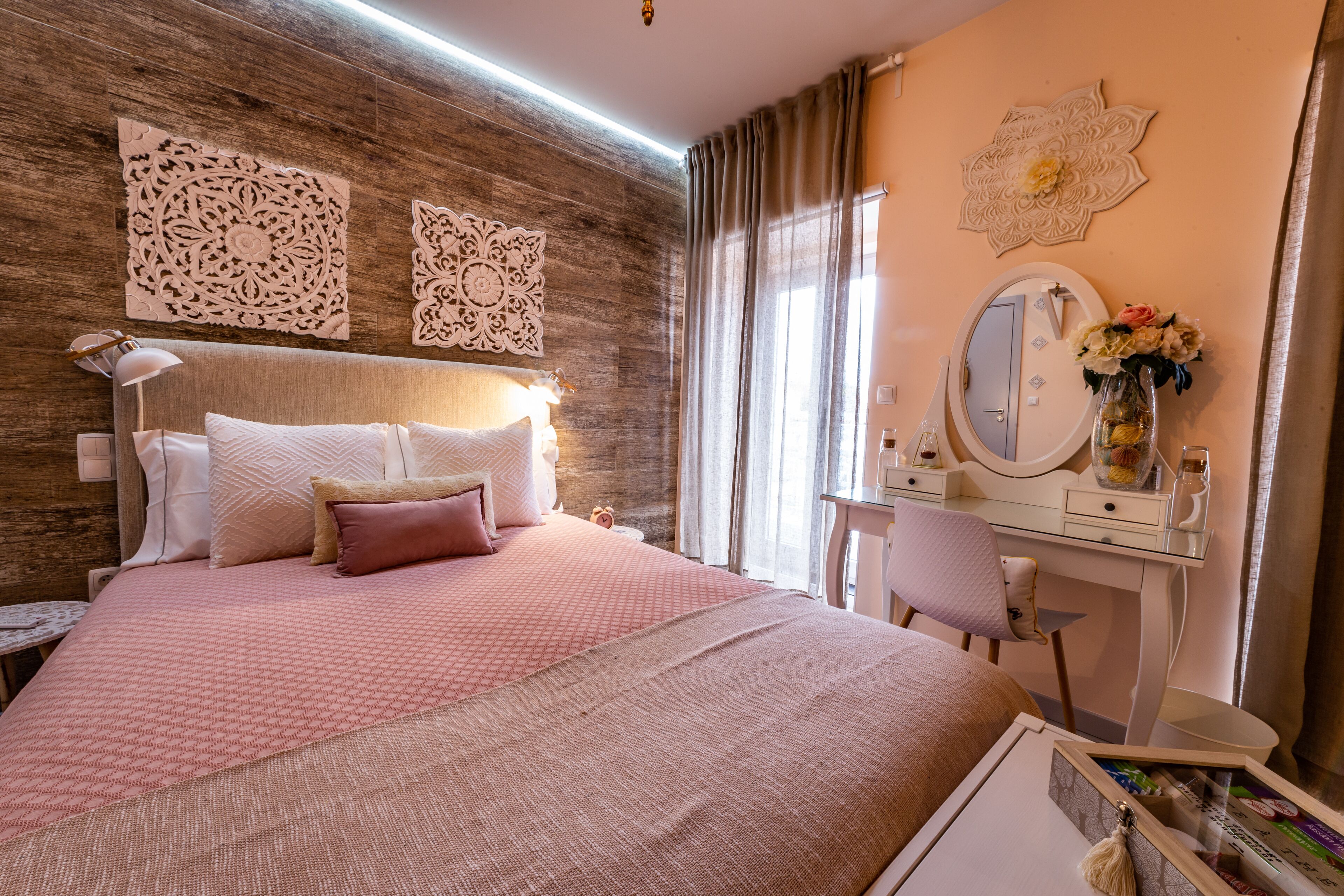 Quarto com cama grande, penteadeira com espelho e arte decorativa na parede.