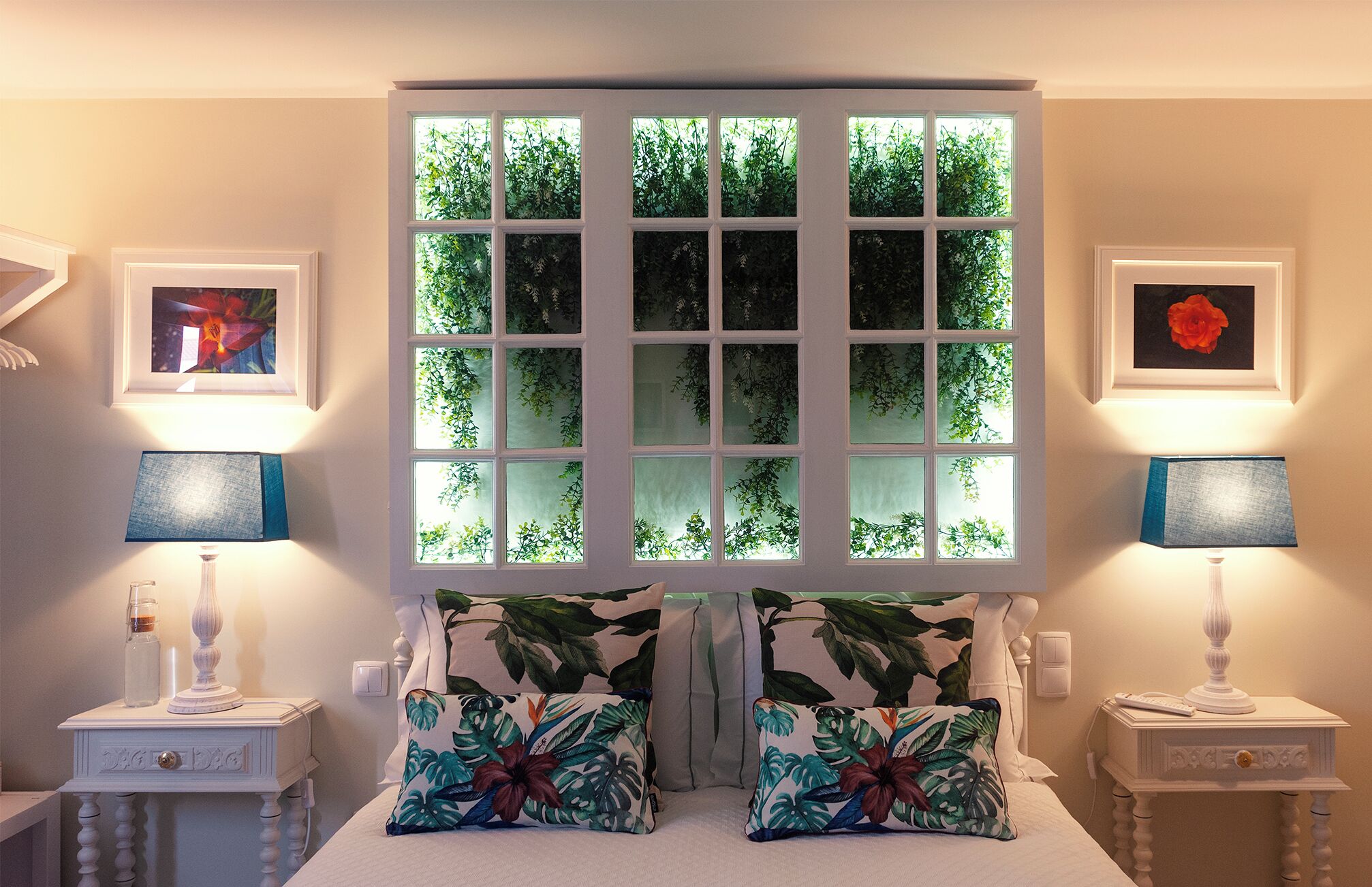 A bedroom with a large window, two bedside tables with lamps, and floral-patterned pillows.