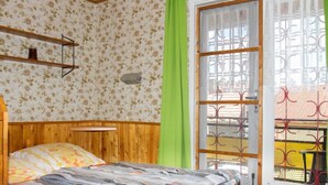 A bedroom with a wooden headboard, a bed with a patterned bedspread, a green curtain, and a window with a metal gate.