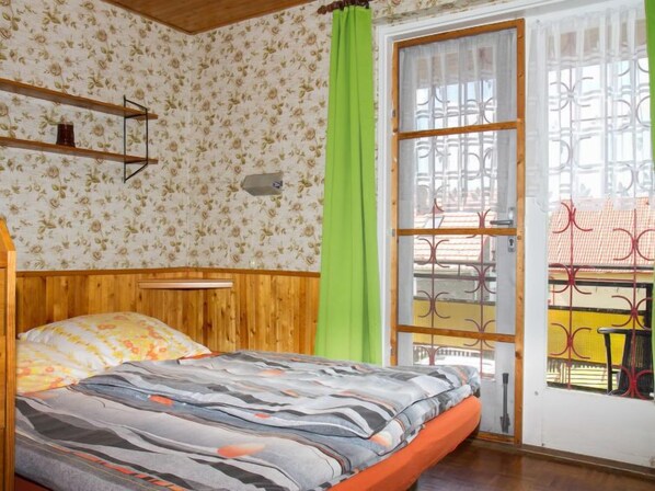 A bedroom with a wooden headboard, a bed with a patterned bedspread, a green curtain, and a window with a metal gate. - Vacation home Pino by Interhome (Balatonboglar)