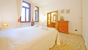 A bedroom with a large bed, a wooden dresser, a radiator, and a window with curtains. - DolceVita Apartments N. 331 (Venice)