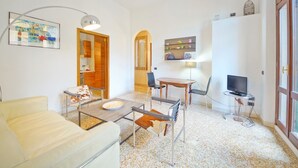 A modern living room with a sofa, a dining table, chairs, a TV, and a kitchen area with cabinets and a microwave. - DolceVita Apartments N. 331 (Venice)